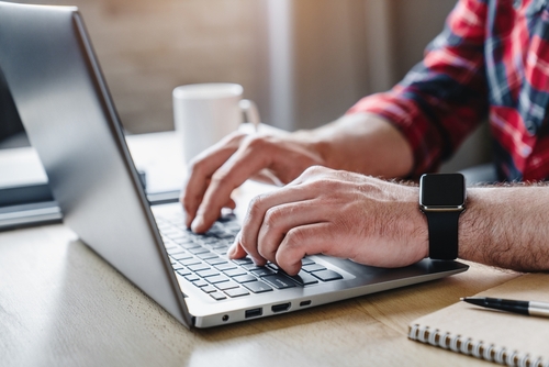 Cropped shot of man's hands using laptop at home office. Hands of adult contemporary office manager over laptop keypad during work over new business project by table